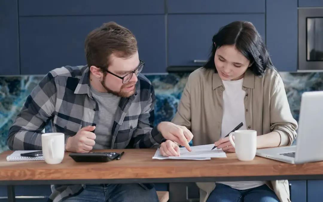 A young couple reviewing financial documents together at home to plan their first mortgage.