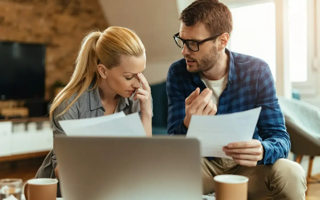 Stressed couple reviewing financial documents and bills at home after missing a mortgage payment.